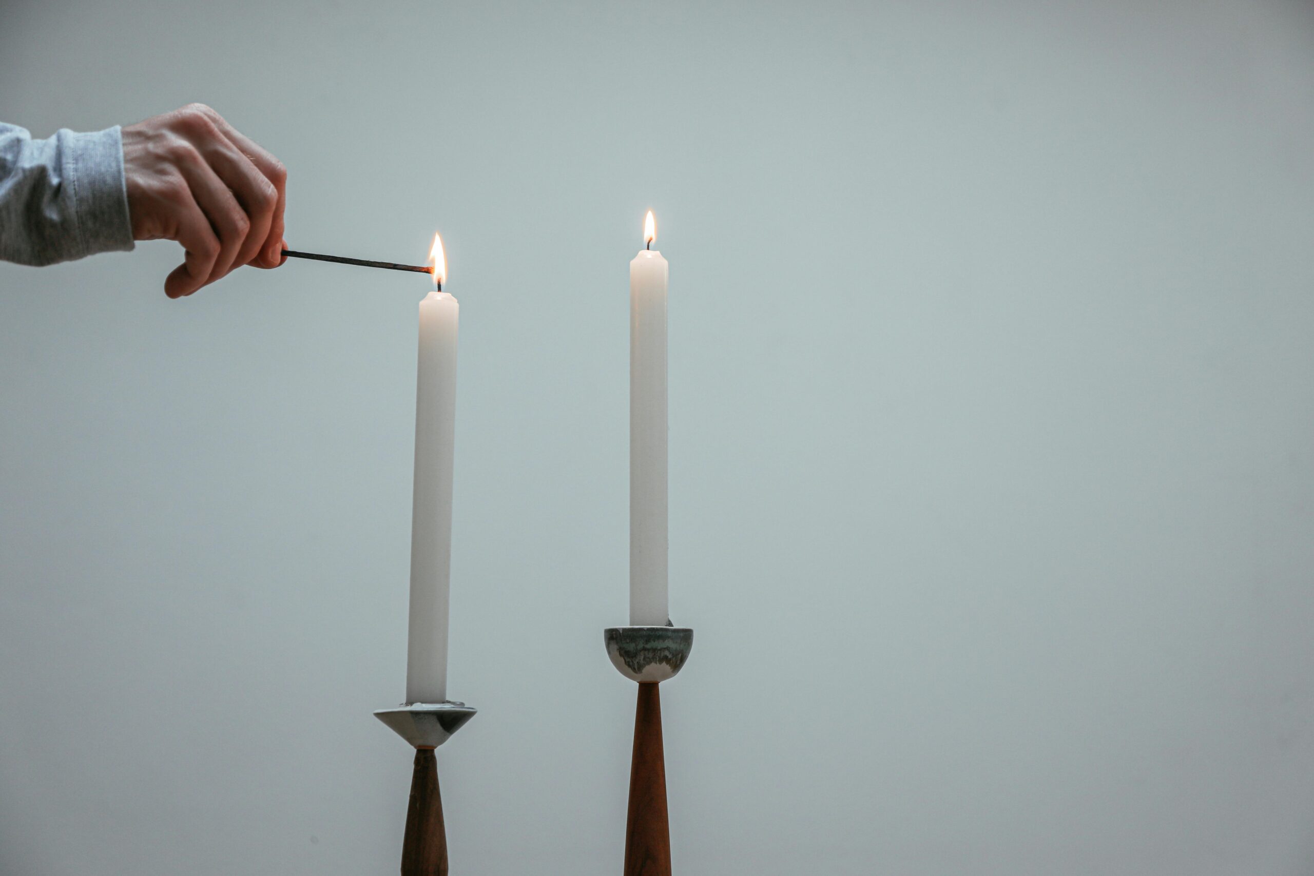 Man's hand lighting two taper candles with a match, symbolizing the passing of light and legacy.